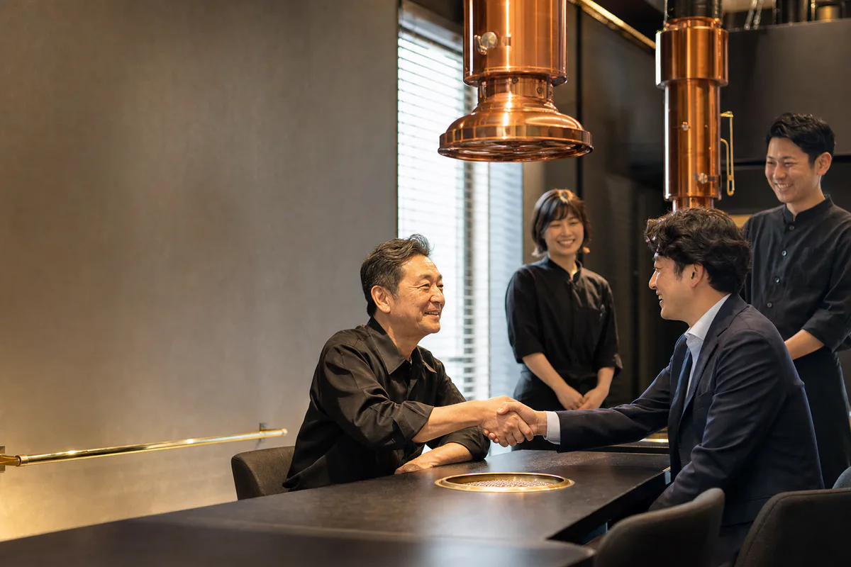 焼肉店の引き継ぎについて握手を交わす現経営者と次の運営者